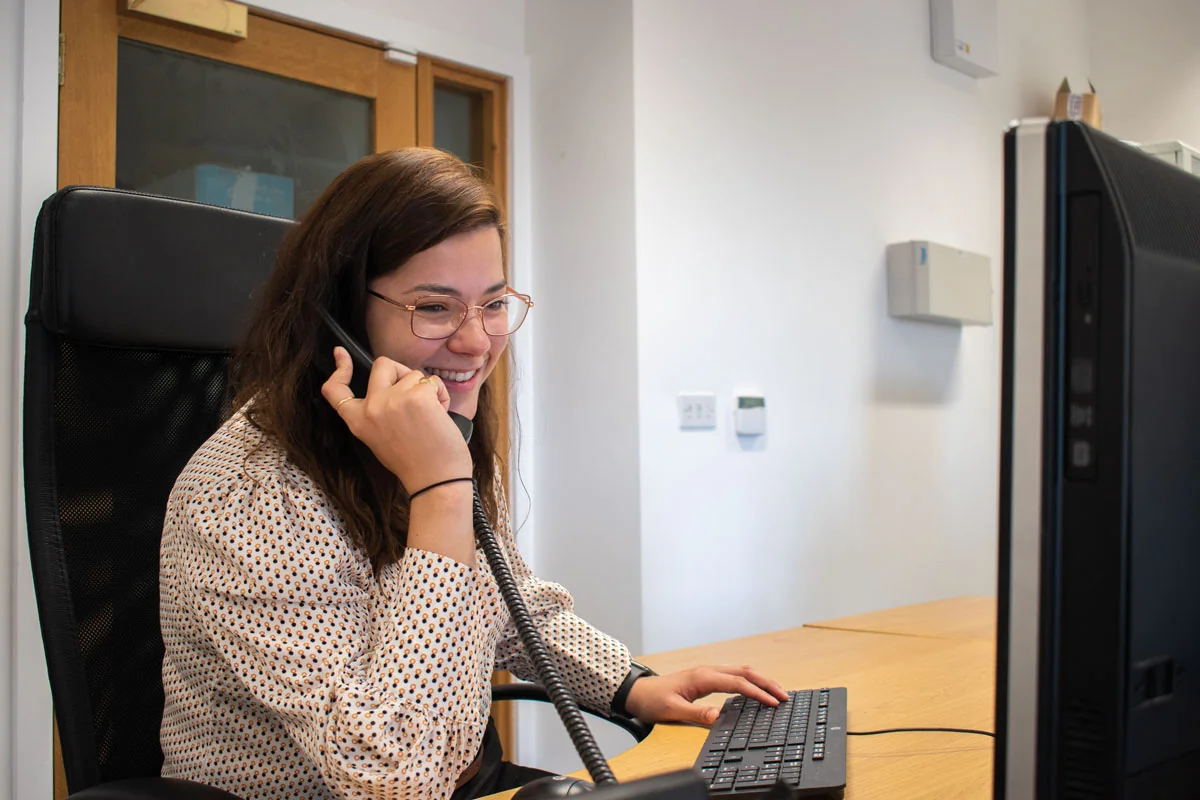 A dental receptionist smiling while taking a patient call at her desk